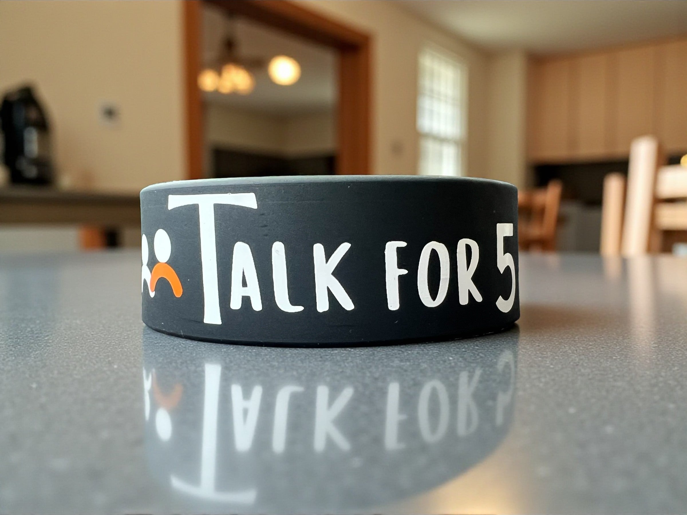Classic Talk For 5 wristband, comfortable and minimalistic product with a Talk For 5 logo, displayed n a dining table