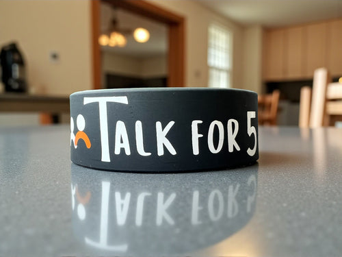 Classic Talk For 5 wristband, comfortable and minimalistic product with a Talk For 5 logo, displayed n a dining table