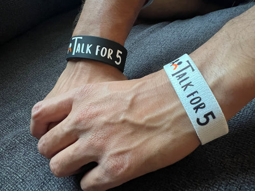 Man wearing Talk for 5 conversation starter wristbands one on each hand.