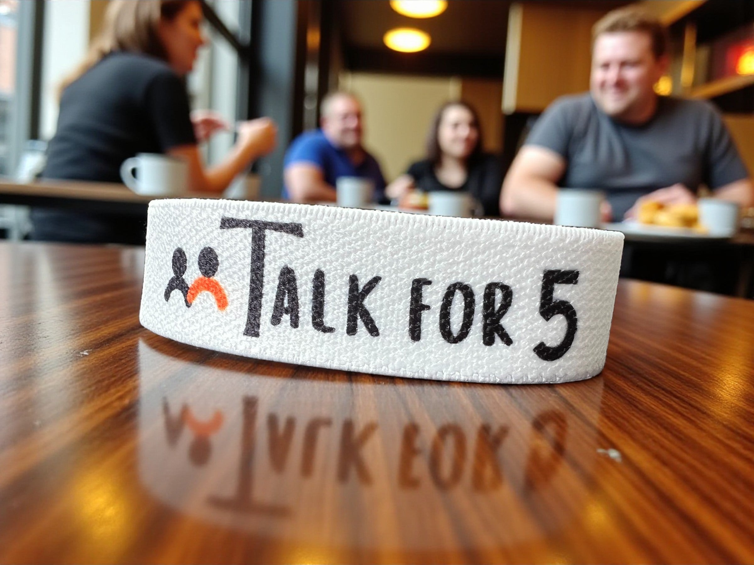 White band with 'Talk For 5' text on a wooden table in a casual setting
