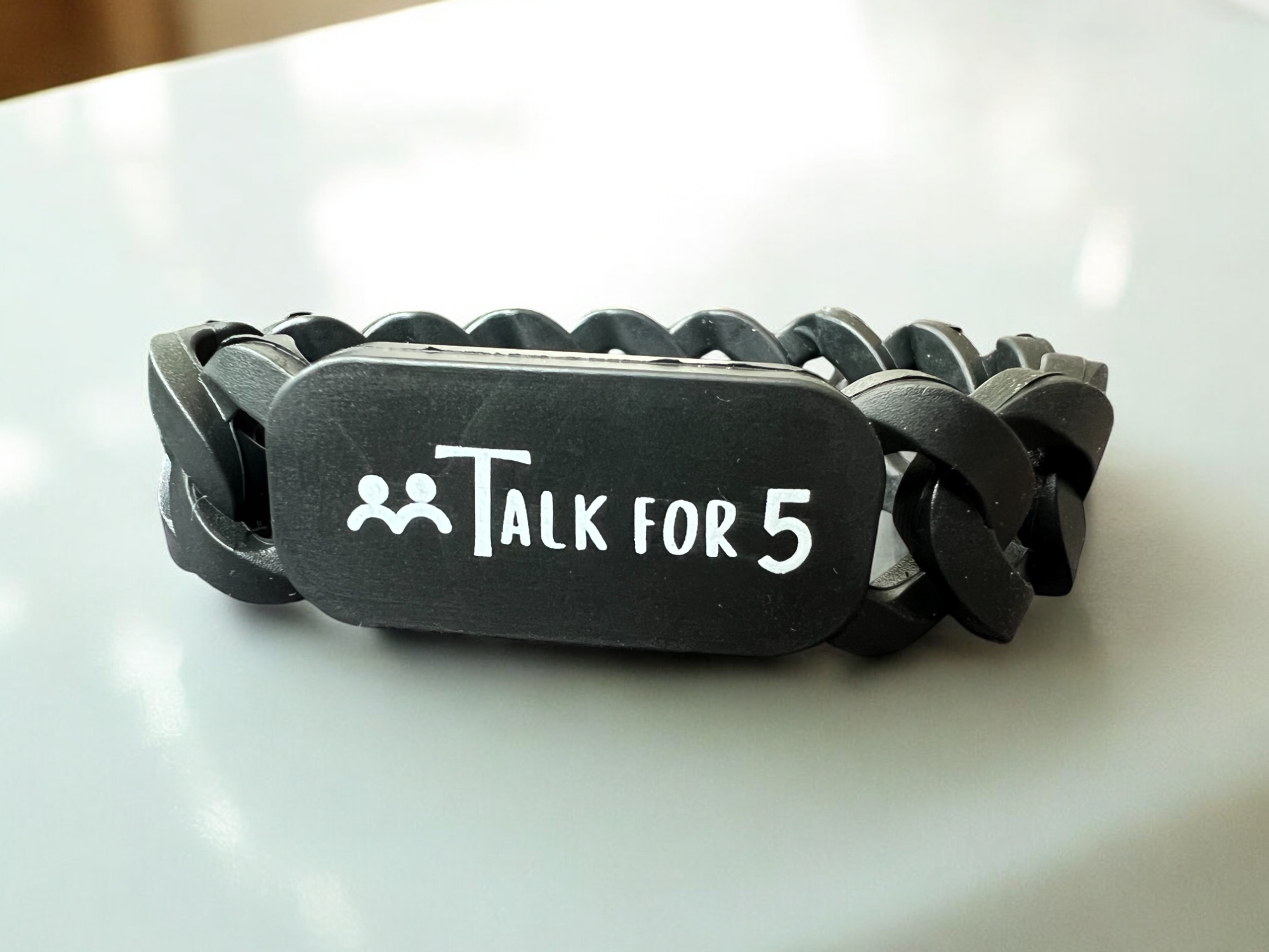 Black bracelet with a subtle design, a 'Talk For 5' logo on a white surface